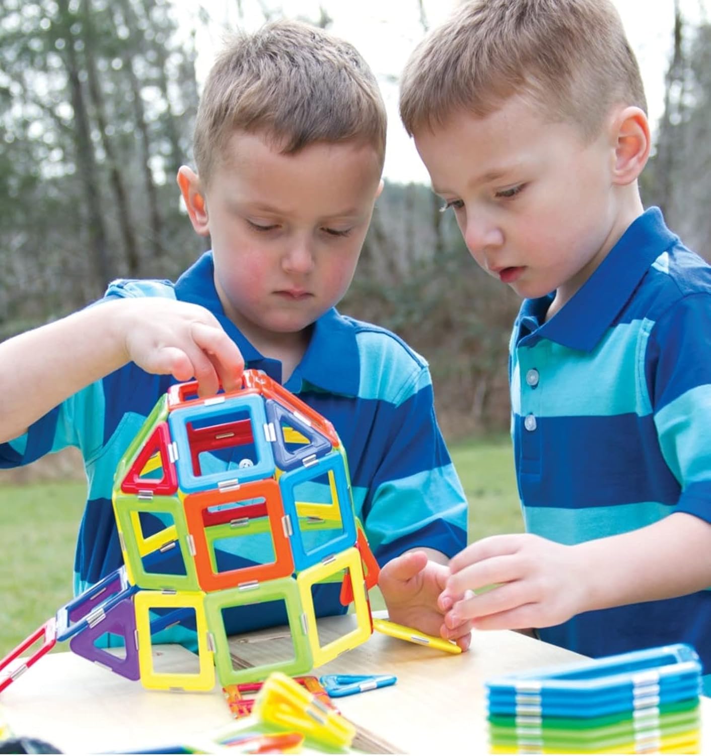 "Two children assembling the GeoSmart Solar Spinner, connecting colorful magnetic geometric pieces to build the solar-powered spinning mechanism, engaging in hands-on STEM learning.