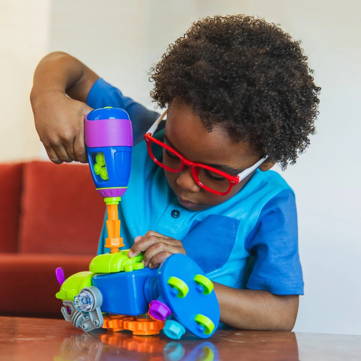 Young boy using the kid-friendly screwdriver to assemble and customize a robot from the Design & Drill Robot Workshop. Hands-on STEM learning from Learning Resources.