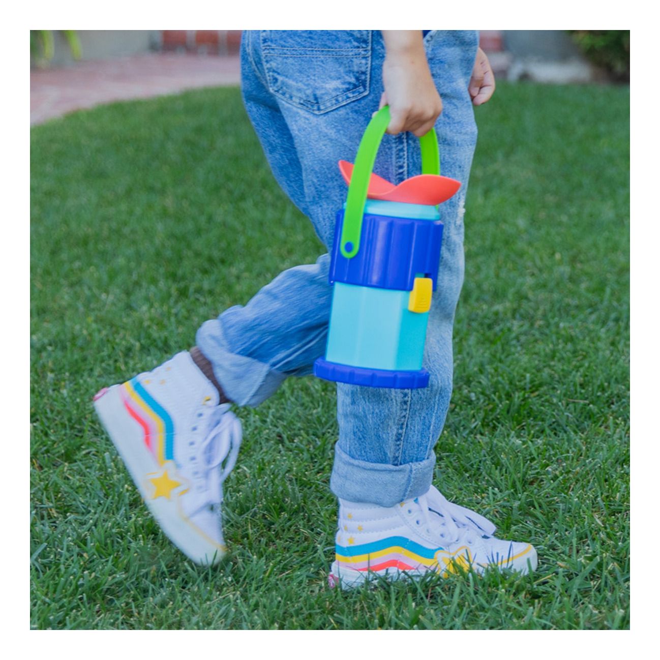 A child walking across the grass, holding GeoSafari Jr. Rocknoculars by the sturdy handle, ready for an STEM toy, educational, outdoor exploration adventure.