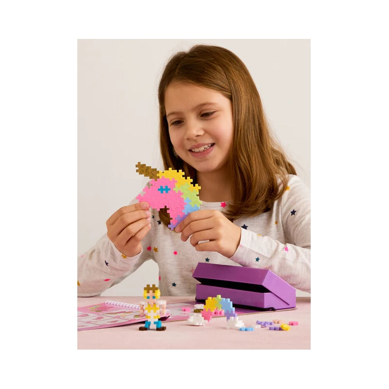 "A girl holding a completed Plus-Plus unicorn head, with a small Plus-Plus figure resting on the desk, showcasing creative play and hands-on STEM learning