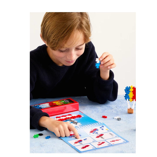 "A child following the Plus-Plus Transport Activity Pad instructions, carefully assembling a colorful vehicle model using interlocking pieces.
