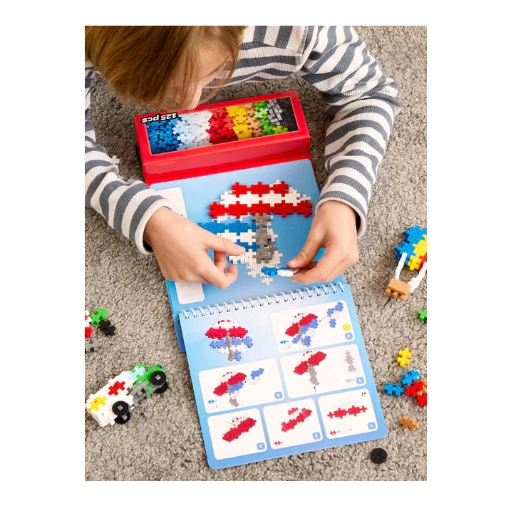 A close-up of a child following the Plus-Plus Transport Activity Pad instructions, carefully assembling a colourful vehicle model using interlocking pieces