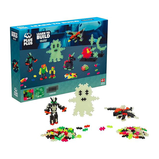 The Plus-Plus Learn to Build Glow-in-the-Dark box with three built models, including a glowing ghost, and loose interlocking pieces in front.