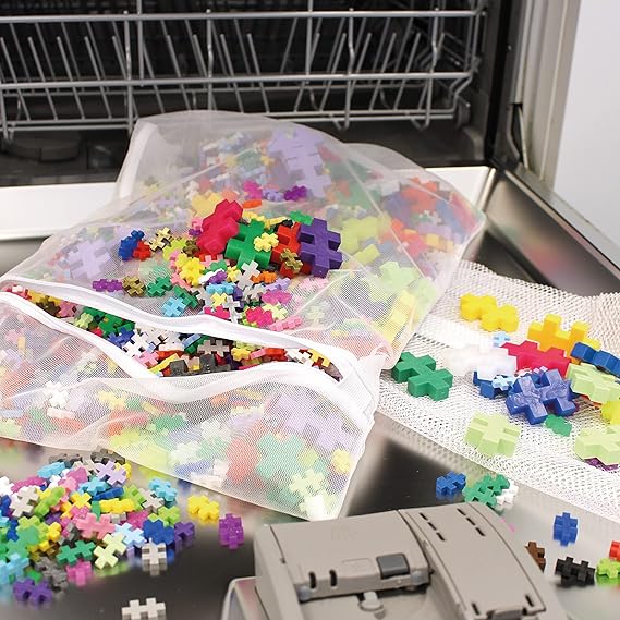 A mesh bag filled with Plus-Plus interlocking pieces being placed into a dishwasher, with a few loose pieces nearby, showing an easy cleaning method.