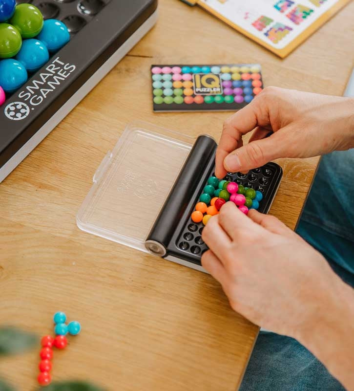 "An adult engaging with SmartGames IQ Puzzler Pro, carefully placing colorful puzzle pieces onto the compact game board to solve a logic-based challenge.