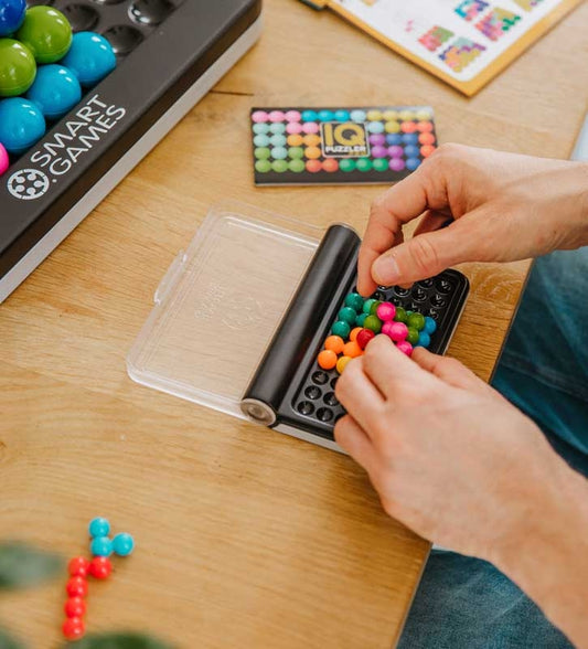 "An adult engaging with SmartGames IQ Puzzler Pro, carefully placing colorful puzzle pieces onto the compact game board to solve a logic-based challenge.