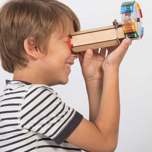A boy holding and looking through a fully assembled Smartivity Kaleidoscope, observing coloruful patterns created by the reflection of beads and mirrors inside the STEM toy