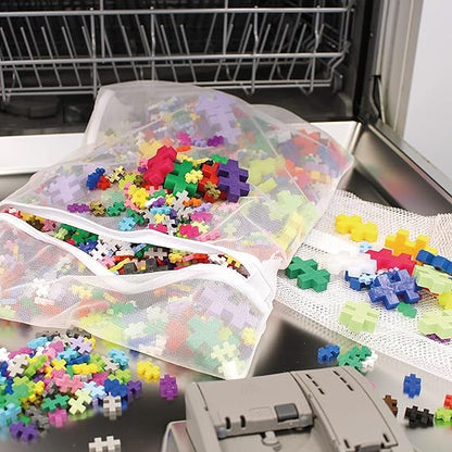 A mesh bag filled with Plus-Plus interlocking pieces being placed into a dishwasher, with a few loose pieces nearby, showing an easy cleaning method.