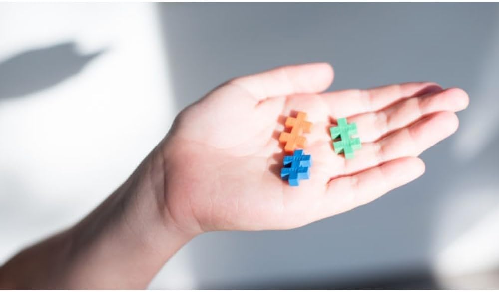 A hand holding three colourful Plus-Plus interlocking pieces in its palm, showcasing their unique shape and versatility for creative building