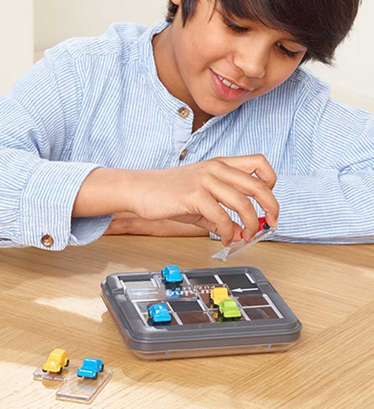A boy focused on solving a challenge in the SmartGames Parking Puzzler, carefully placing colorful car pieces on the compact game board to complete the logic puzzle.